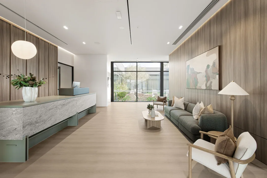 Reception lobby with a long grey stone counter on a sage-green base, timber wall panelling and a grey sofa opposite.