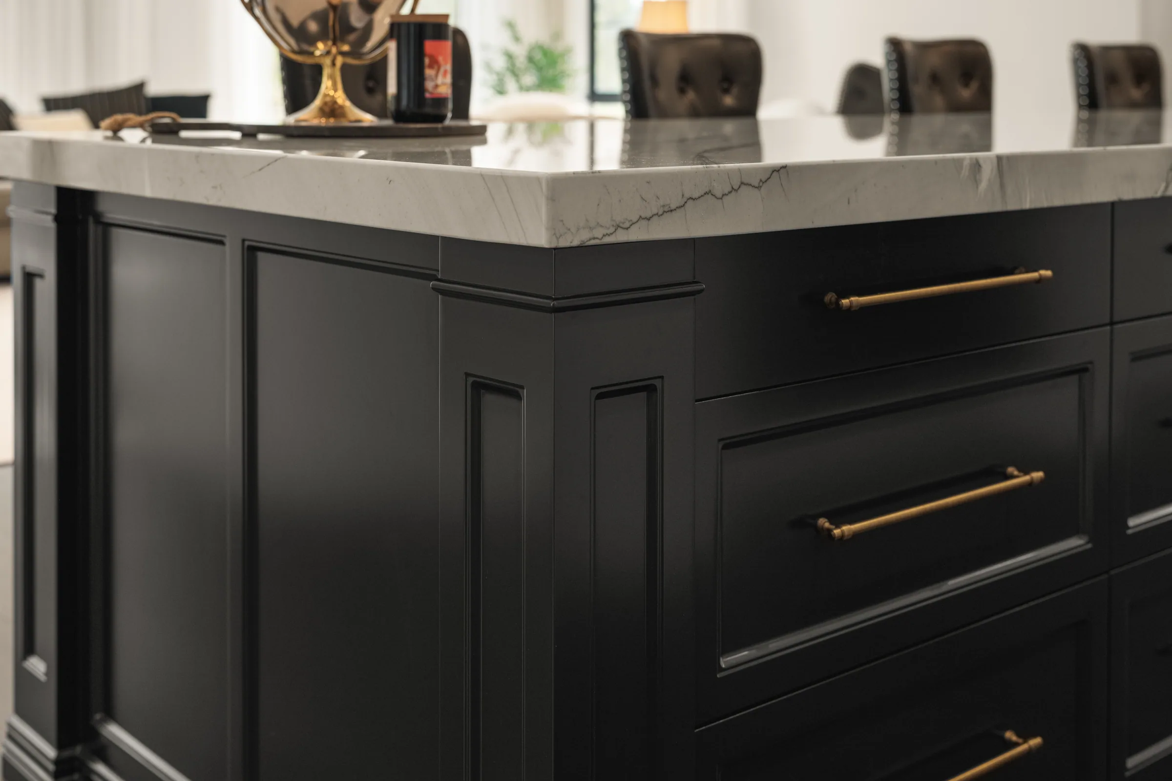 Corner of the black island showing raised panel end, pilaster detail, brass drawer pulls and the veined stone edge.